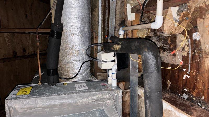 # Condensate Pump Installation with Safety Controls

Completed installation of condensate pump system with dedicated drain pan and float switch for HVAC air handler unit located in attic space. Mounted condensate pump assembly adjacent to existing air handler, ensuring proper positioning for gravity drainage from unit into pump reservoir. 

Installed dedicated safety drain pan beneath air handler to capture overflow or leak conditions. Integrated float switch into pan as secondary safety control to shut down system operation in event of primary drainage failure or pump malfunction. Wired float switch into unit control circuit to interrupt compressor operation when activated.

Routed black insulated refrigerant lines and white PVC condensate discharge piping according to manufacturer specifications. Secured all piping and tubing to floor joists using appropriate fasteners to prevent movement and ensure proper pitch for drainage. Connected condensate drain line from air handler coil to p