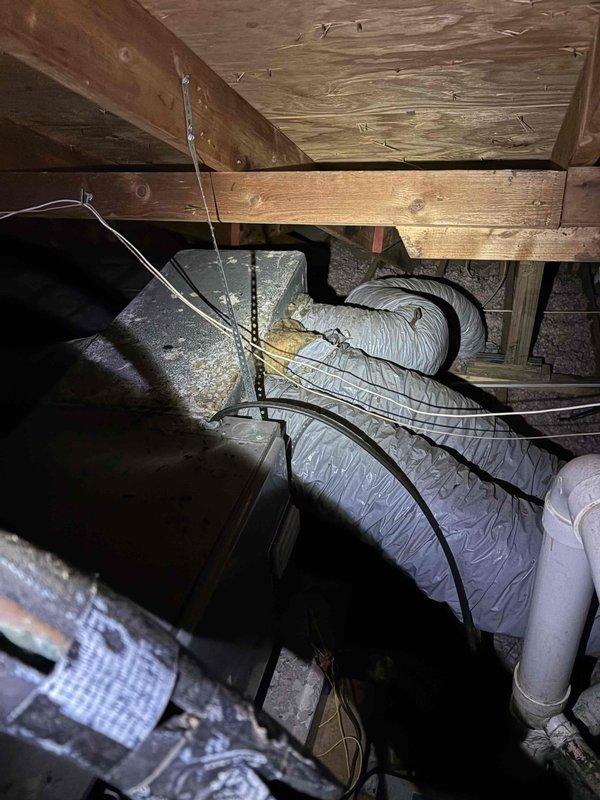 Responded to service call for air conditioning system blowing warm air at vacant property. Upon arrival, accessed property using lockbox and confirmed system had been turned off by occupants. Performed diagnostic inspection of HVAC system including attic-mounted ductwork and air handler components. Inspected flexible ductwork runs throughout attic space, verifying proper installation, support, and insulation integrity. Examined air filtration system and confirmed clean filter installation in return air housing. Documented all accessible system components including ductwork routing, connections, insulation wrapping, and structural mounting points. Photographed attic installation showing yellow flexible supply ducts, pink fiberglass insulation near roof decking, and multiple gray insulated duct runs secured to wooden framing members. System requires further evaluation to determine root cause of warm air discharge issue.