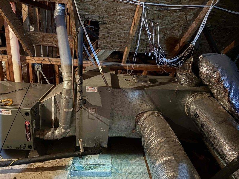 Responded to no-cooling complaint on one of two residential HVAC systems serving kitchen, living room, and front bedroom areas. Upon arrival, unit was turned off by homeowner due to warm air discharge. Performed diagnostic inspection revealing severely clogged evaporator coil with heavy accumulation of dirt, dust, and debris throughout coil fins, particularly concentrated in central areas. Documented condition of 2005-era equipment showing significant lack of recent maintenance. Inspected attic-mounted air handler unit and associated ductwork system. Presented membership program options to customer for ongoing maintenance needs.
