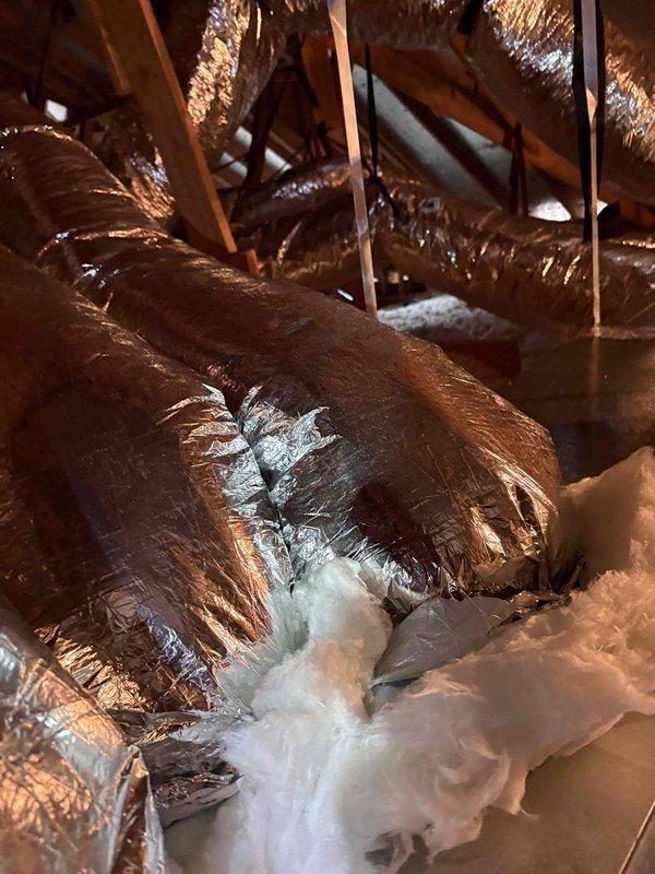 Performed quality assurance inspection on recently installed Amana HVAC system due to concerns about excessive runtime and increased utility consumption. Upon inspection, discovered significant damage to attic ductwork including torn metallic vapor barrier wrapping with exposed fiberglass insulation, and improperly installed flexible ductwork that was compressed and inadequately supported throughout the attic space. These deficiencies were causing substantial air leakage and reduced system efficiency, resulting in extended equipment runtime to maintain temperature setpoints. Documented all findings with photographs and obtained required manufacturer paperwork signatures from homeowner.