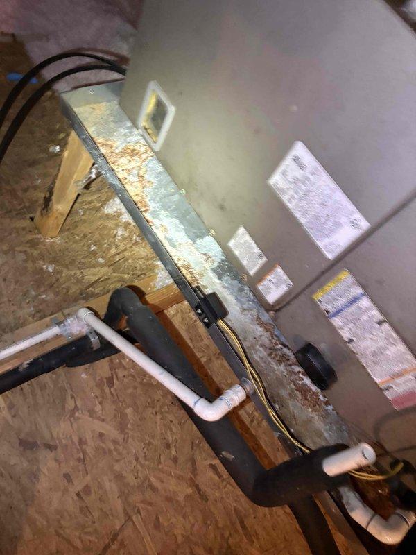 Responded to service call for frozen AC unit that had been shut down for several days. Upon arrival, conducted diagnostic inspection of HVAC system located in mechanical room. Observed air handler equipment with visible control panels and ductwork connections. Noted signs of moisture intrusion and water damage in the mechanical space, including rust-colored staining at door threshold and corrosion on metal surfaces, indicating previous condensation or drainage issues. Inspected attic installation area where condensate drain system and associated PVC piping were observed. Examined drain line routing and electrical connections to air handler. Identified potential contributing factors to freezing condition, including evidence of moisture accumulation in the system area. Documented equipment condition and surrounding environment through photographic evidence showing water damage patterns and system installation configuration. Recommended addressing drainage concerns and monitoring for prop