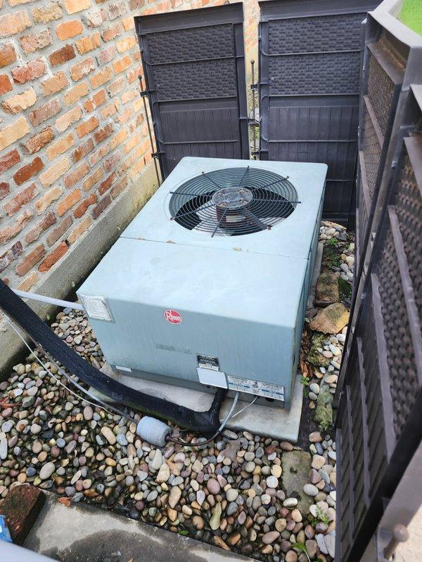 Responded to after-hours dispatch for reported clunky noise from outdoor HVAC unit, suspected fan motor issue. Upon arrival, inspected Rheem condensing unit located in side yard between brick wall and privacy fence. Performed diagnostic testing of electrical components using clamp meter, measuring amperage draw at 6.86 amps. Evaluated condenser fan motor operation, capacitor condition, and compressor function. Identified source of abnormal noise and assessed system for potential damage. Documented equipment condition with photos of exterior unit and internal electrical components for service records.