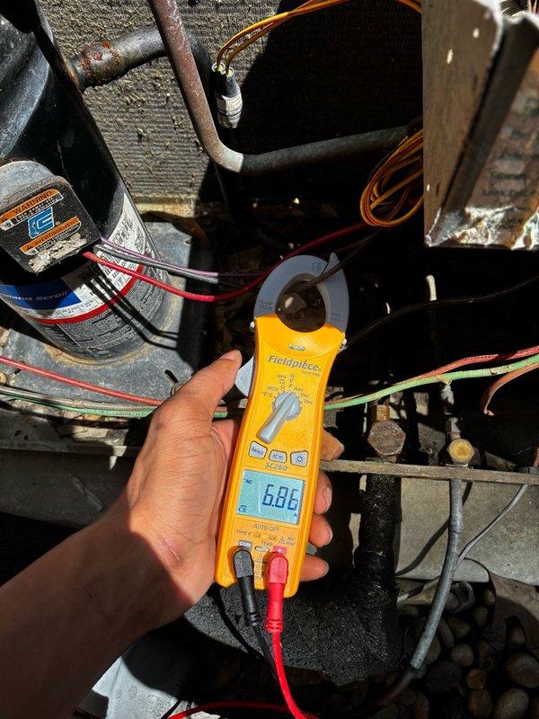 Responded to after-hours dispatch for reported clunky noise from outdoor HVAC unit, suspected fan motor issue. Upon arrival, inspected Rheem condensing unit located in side yard between brick wall and privacy fence. Performed diagnostic testing of electrical components using clamp meter, measuring amperage draw at 6.86 amps. Evaluated condenser fan motor operation, capacitor condition, and compressor function. Identified source of abnormal noise and assessed system for potential damage. Documented equipment condition with photos of exterior unit and internal electrical components for service records.