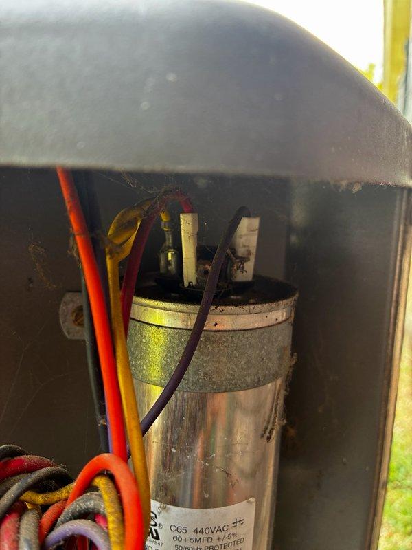 Responded to no cooling call on 2009 HVAC system with condenser unit not operating. Upon arrival, confirmed air handler running properly while outdoor unit failed to start. Performed diagnostic inspection of condenser unit and identified failed capacitor as root cause of system failure. Photographed capacitor showing visible signs of aging, discoloration, and deterioration with multiple wire connections intact. Inspected electrical connections and verified proper wiring configuration. Observed significant rust and corrosion throughout outdoor unit framework and coil assembly, indicating extended exposure to environmental elements and moisture. Heat exchanger fins appeared relatively clean despite advanced corrosion on surrounding metal supports and brackets. Discussed membership program options with customer for consideration.