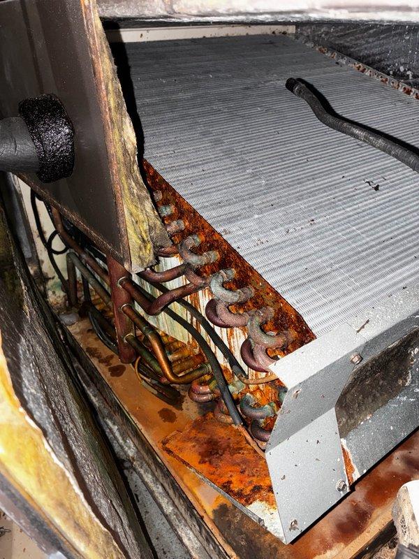 Responded to no cooling call on 2009 HVAC system with condenser unit not operating. Upon arrival, confirmed air handler running properly while outdoor unit failed to start. Performed diagnostic inspection of condenser unit and identified failed capacitor as root cause of system failure. Photographed capacitor showing visible signs of aging, discoloration, and deterioration with multiple wire connections intact. Inspected electrical connections and verified proper wiring configuration. Observed significant rust and corrosion throughout outdoor unit framework and coil assembly, indicating extended exposure to environmental elements and moisture. Heat exchanger fins appeared relatively clean despite advanced corrosion on surrounding metal supports and brackets. Discussed membership program options with customer for consideration.