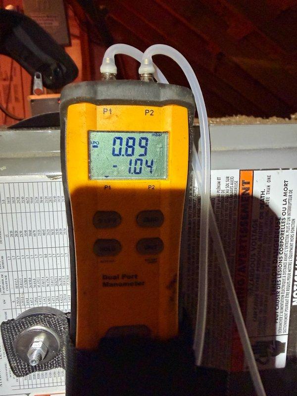 Responded to callback for recurring condensate pan filling issue on same unit from recent service visit. Upon arrival, performed diagnostic pressure testing using digital manometer, which revealed readings of 0.89 and -1.04, indicating potential airflow restriction or drainage obstruction. Inspection of attic-installed HVAC system revealed heavily soiled flexible ductwork and components with significant dust and debris accumulation throughout the system. Documented existing conditions with photos showing substantial particulate buildup on main supply duct, rigid duct sections, and surrounding components. Assessment indicates compromised system cleanliness may be contributing to condensate drainage problems. Customer had temporarily removed water from pan overnight prior to service call.