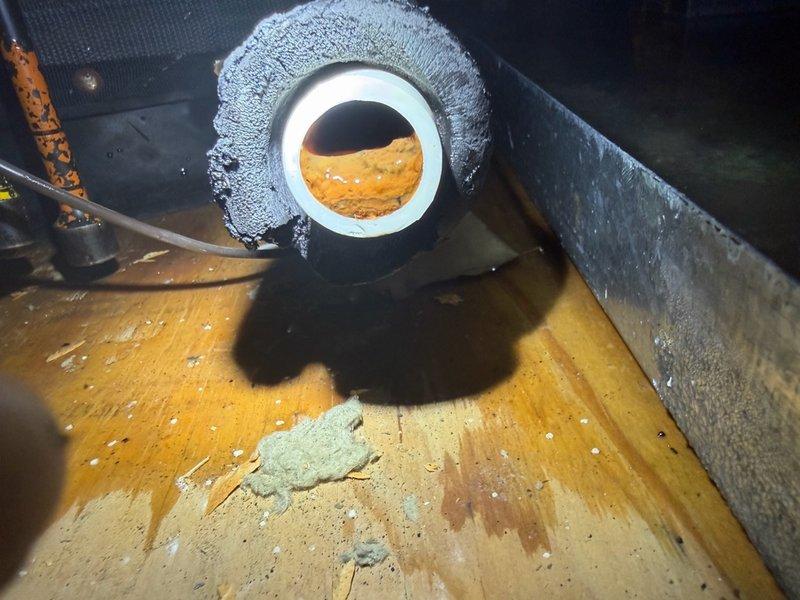 # After Hours Emergency Dispatch

Responded to emergency call regarding full overflow drain pan. Upon arrival, advised customer to shut down system immediately to prevent water damage. Inspection revealed severe frost buildup on refrigerant lines indicating restricted airflow or low refrigerant charge. Documented heavy accumulation of dirt, debris, and organic material on outdoor condenser unit components, which was likely contributing to system malfunction. Observed water staining on wooden platform and surrounding areas consistent with ongoing condensation issues. Unit age estimated at 15+ years based on installation timeframe provided. Photographed frozen evaporator components and contaminated condenser coil for documentation purposes. Recommended immediate follow-up service appointment for thorough system cleaning, refrigerant charge verification, and drain line clearing to restore proper operation and prevent further water overflow.