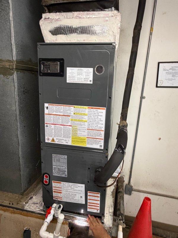Completed installation of 2-ton split system HVAC unit including outdoor condenser and indoor air handler. Condenser unit positioned on concrete pad against exterior brick wall with proper clearance and secured electrical disconnect. Air handler installed in basement utility area with appropriate ductwork connections and condensate drainage. All electrical conduit properly routed and secured to building exterior. System installation includes manufacturer labeling, safety warnings, and operational specifications clearly visible on equipment. Unit tested and verified operational upon completion.