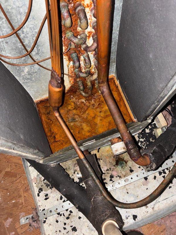 # Dispatch Summary

Responded to cooling complaint with unit experiencing daily temperature rise and intermittent freeze-ups. Upon arrival, conducted visual inspection of HVAC system revealing extensive rust and corrosion on refrigerant lines, mounting brackets, and condensate pan. Heavy oxidation present on copper piping connections and metal framework, indicating prolonged moisture exposure. Documented equipment condition with photographs showing significant deterioration of components including corroded drip pan, oxidized copper lines, and rusted support structures. Unit requires further diagnostic evaluation to determine root cause of cooling issues and assess impact of corrosion on system performance and refrigerant integrity.