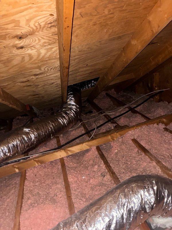 Completed major duct leak repair in attic space. Located and assessed damaged flexible HVAC ductwork showing significant compression and deterioration of metallic exterior surface. Repaired compromised sections of silver flex duct to restore proper airflow and system efficiency. Work performed in attic with pink fiberglass insulation between joists, ensuring all repairs were properly sealed and secured to prevent future air loss.