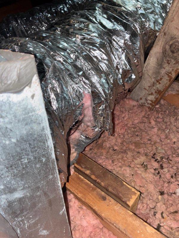 Completed major duct leak repair in attic space. Located and assessed damaged flexible HVAC ductwork showing significant compression and deterioration of metallic exterior surface. Repaired compromised sections of silver flex duct to restore proper airflow and system efficiency. Work performed in attic with pink fiberglass insulation between joists, ensuring all repairs were properly sealed and secured to prevent future air loss.