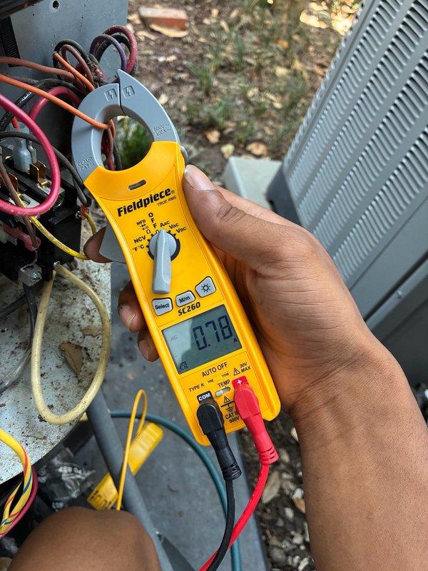 Responded to after-hours dispatch for downstairs air conditioning system blowing warm air while upstairs system operated normally. Performed diagnostic testing on outdoor condensing unit, including electrical measurements of capacitor and motor components using clamp meter. Inspected internal electrical compartment, evaluating capacitor condition, wiring connections, and motor operation. Measured amperage draw at 0.78 amps on system components to assess operational status and identify cooling failure cause.