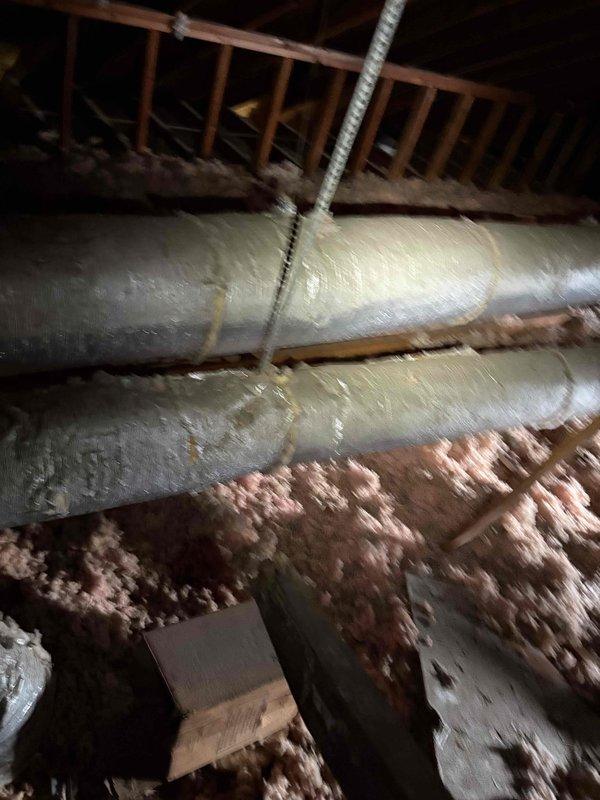 Responded to after-hours dispatch for no cooling complaint with indoor temperature at 74°F and thermostat set to 70°F. Accessed attic-mounted air handler unit and inspected HVAC system components, including ductwork and equipment condition. Documented existing installation showing air handler with accumulated dust and debris, reflective insulated supply ducts, and pink fiberglass batt insulation between joists. System had previous refrigerant service during last cooling season, indicating potential recurring leak or compressor issue requiring further diagnostic evaluation during regular business hours when customer becomes available.