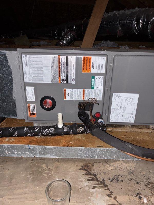 Responded to no cooling complaint with warm air discharge from HVAC system. Instructed customer to switch thermostat from cooling mode to fan-only operation to address potential evaporator coil freeze condition. Documented air handler unit installation in attic space, including refrigerant lines, electrical connections, and drainage components. Observed drain pan with visible staining and discoloration indicating previous moisture accumulation. Photographed evaporator coil assembly and associated piping for service records.