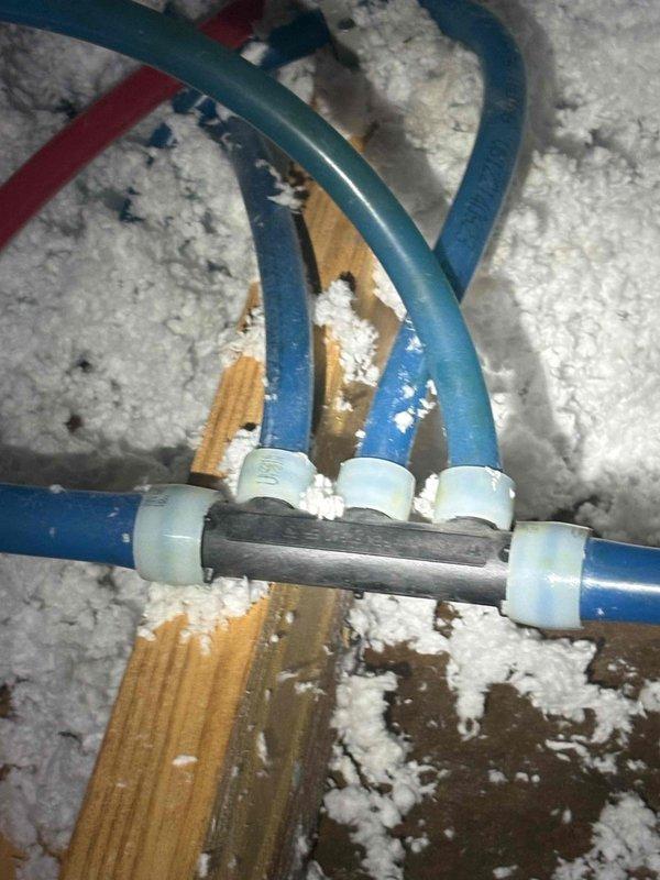 Responded to report of water leaking on ceiling in guest bathroom. Upon inspection, located condensate drain line issue in attic space above affected area. Found PVC drain lines and condensate piping with connections at central junction point surrounded by insulation on structural beam. Both HVAC systems were operating and cooling properly at time of visit. Documented piping configuration and drain line assembly with photos for reference.