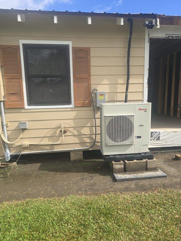Conducted site assessment of existing Amana outdoor HVAC condenser unit to evaluate feasibility of relocation. Documented current installation configuration, including unit placement on concrete block platform, refrigerant line routing along exterior wall, and electrical conduit connections extending to roofline. Photographed existing setup showing proximity to window with shutters and adjacent garage area to determine clearance requirements and potential relocation options for improved placement or accessibility.