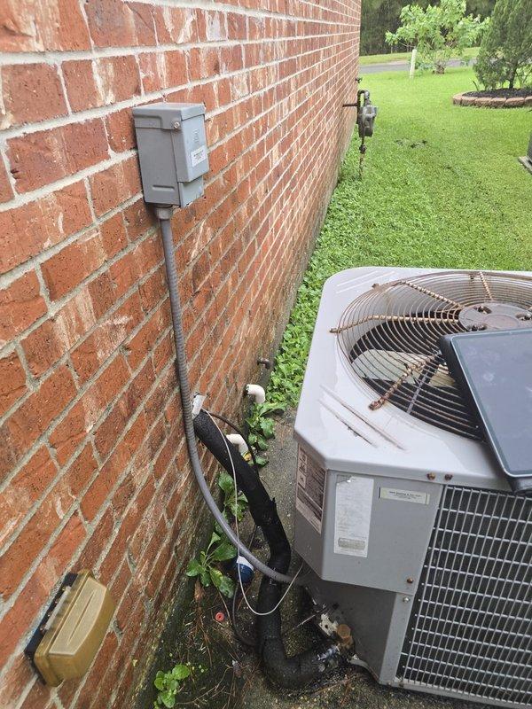 Responded to service call for non-operational air conditioning condenser unit. Upon arrival, inspected existing outdoor HVAC system positioned on concrete pad against exterior brick wall. Unit features gray metal construction with protective grille covering and electrical disconnect box mounted above with conduit connections. Assessed current condenser condition and surrounding installation components including concrete pad, electrical connections, and refrigerant line routing. Provided estimate for complete condenser replacement as requested, excluding full system replacement options per customer preference.