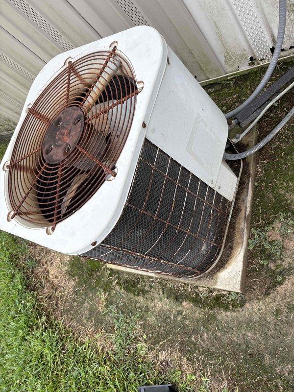 Responded to emergency service call for mobile home HVAC system that experienced smoking incident requiring fire department response. Upon inspection, discovered snail intrusion in blower motor housing causing the reported smoking condition. System originally installed in 2002 and currently non-operational per customer safety concerns. Documented equipment condition showing significant age-related wear on outdoor condenser unit with rust on fan guard and accumulated debris on exterior surfaces.