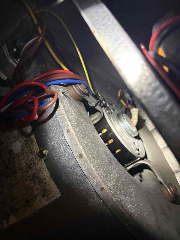 Responded to no-cooling complaint on downstairs system in two-system residence. Unit located on elevated platform approximately 20 feet high, requiring ladder access. Upon inspection of 20+ year-old condenser unit, found capacitor failure as suspected. Photographed and documented blower motor assembly with multiple wire connections and capacitor mounted on gray metal bracket showing significant dirt accumulation and corrosion on surrounding components. System inoperative due to failed capacitor preventing compressor operation. Accessed vacant property using provided lockbox code for entry and assessment.