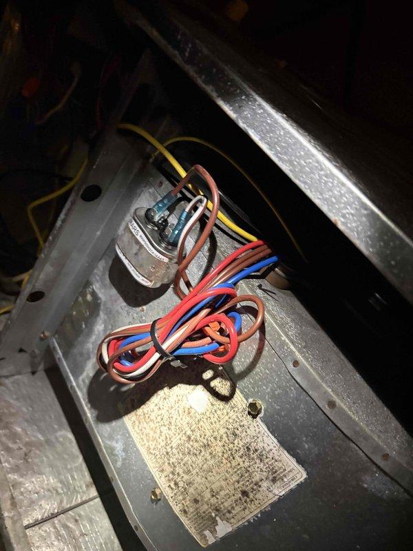 Responded to no-cooling complaint on downstairs system in two-system residence. Unit located on elevated platform approximately 20 feet high, requiring ladder access. Upon inspection of 20+ year-old condenser unit, found capacitor failure as suspected. Photographed and documented blower motor assembly with multiple wire connections and capacitor mounted on gray metal bracket showing significant dirt accumulation and corrosion on surrounding components. System inoperative due to failed capacitor preventing compressor operation. Accessed vacant property using provided lockbox code for entry and assessment.