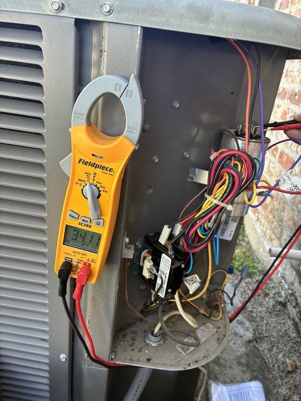 Performed an AC tune-up on a single-system installation, inspecting the condenser's electrical compartment and testing the run capacitor, contactor, and wiring with a clamp meter (34.1 reading recorded), and noted light corrosion and debris on the lower condenser tray. Documented water staining and a split in the painted ceiling drywall in the kitchen, consistent with a prior moisture issue that had been painted over and never resolved, and recommended further evaluation of the evaporator coil, condensate drain line, and secondary drain pan to identify the source of the leak.