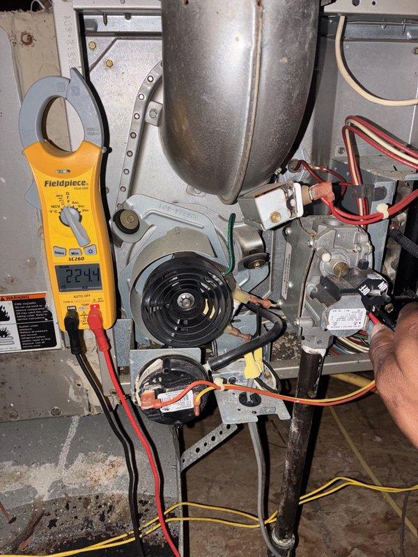 Performed a heater tune-up including cleaning and inspection of the gas furnace with the access panel removed. Verified electrical operation using a clamp meter, checking amperage on the supply wiring and testing voltage at the gas valve, and inspected the inducer motor, pressure switch, flue assembly, and wiring connections for proper condition and function.