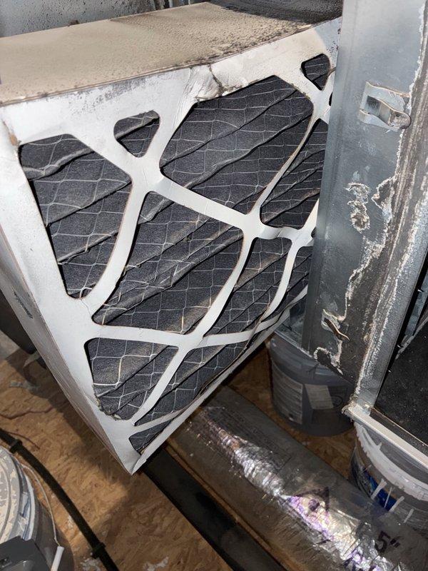 Performed AC tune-up on electric split system in response to elevated utility bills and uneven cooling. Inspected the attic air handler and found the return plenum and insulated duct surfaces heavily coated with dust and lint, and the pleated filter loaded with soot and debris with worn frame edges, restricting airflow. Removed the dirty filter, cleaned accumulated debris from the plenum and housing, and verified the system for proper airflow to help improve efficiency and temperature balance to the warmer side of the home.