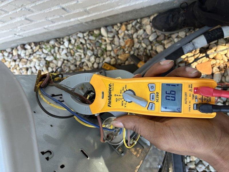 Responded to reports of a clogged condensate drain line and a non-communicating thermostat on the upstairs system. Inspected the air handler and found the drain pan heavily rusted and corroded with debris present, and checked electrical components with a clamp meter, measuring 0.61 A on the control wiring. Documented the pan corrosion and thermostat communication fault for further repair and system diagnostics.