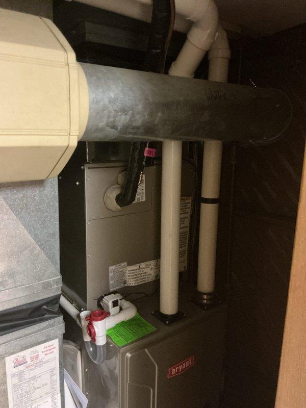 Completed installation of new Bryant air conditioning system including outdoor condenser unit and indoor evaporator coil. Mounted condenser on rubber isolation pad on exterior paver patio at corner of building, ran refrigerant lines vertically along brick wall to connect with indoor coil installed above existing Bryant furnace in mechanical closet. Installed condensate treatment system, verified all electrical connections, tested system operation and confirmed proper cooling performance.