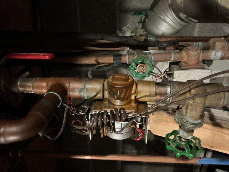 Responded to service call for boiler that would not shut off. Upon inspection, found significant corrosion and verdigris buildup on brass valve components and pipe fittings throughout the boiler system. Identified faulty zone valve with corroded electrical connections and compromised mechanical operation preventing proper system shutdown. Evaluated multiple copper pipe branches with gate valves controlling different heating zones. Noted aging infrastructure with varying degrees of oxidation on copper piping and fittings. Recommended replacement of corroded valve assembly and affected electrical components to restore proper boiler cycling and prevent continuous operation.