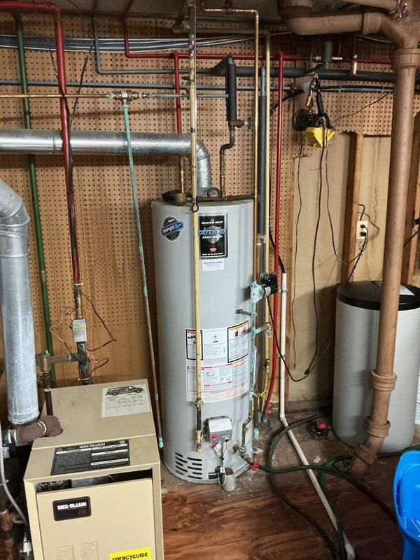 Performed comprehensive water heater tune-up on residential tanked unit located in basement utility area. Conducted thorough inspection of all plumbing connections, including inlet and outlet copper piping, temperature and pressure relief valve, and associated brass fittings at base of unit. Verified proper operation of venting system with metal flue pipe connection to ceiling. Inspected manufacturer labels and specification plates for compliance verification. Examined condition of surrounding plumbing infrastructure including PEX distribution lines mounted to pegboard walls and confirmed adequate clearances around unit per code requirements. All components found to be functioning within normal parameters. Documented equipment condition with photographic records showing water heater installation, mechanical room layout, and plumbing configuration for service history reference.