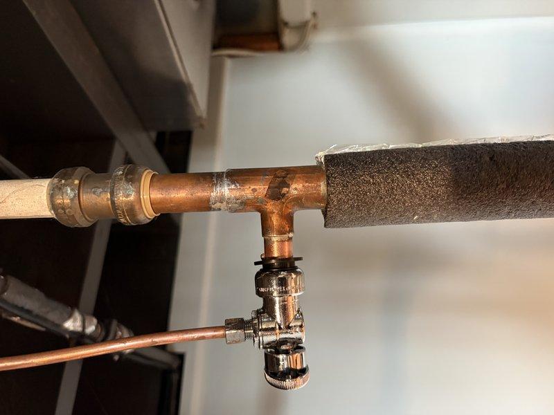 Completed routine HVAC maintenance tune-up on a 6-year-old furnace system that was operating properly. Performed standard inspection and preventative maintenance procedures. Documented existing copper piping configuration with T-joint fittings and compression connectors, noting foam pipe insulation in place. Observed significant corrosion and material degradation on metal component near pipe junction, indicating long-term moisture exposure that will require monitoring or future repair consideration. System remains operational following tune-up service.