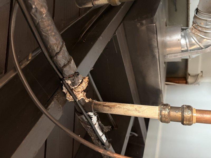 Completed routine HVAC maintenance tune-up on a 6-year-old furnace system that was operating properly. Performed standard inspection and preventative maintenance procedures. Documented existing copper piping configuration with T-joint fittings and compression connectors, noting foam pipe insulation in place. Observed significant corrosion and material degradation on metal component near pipe junction, indicating long-term moisture exposure that will require monitoring or future repair consideration. System remains operational following tune-up service.