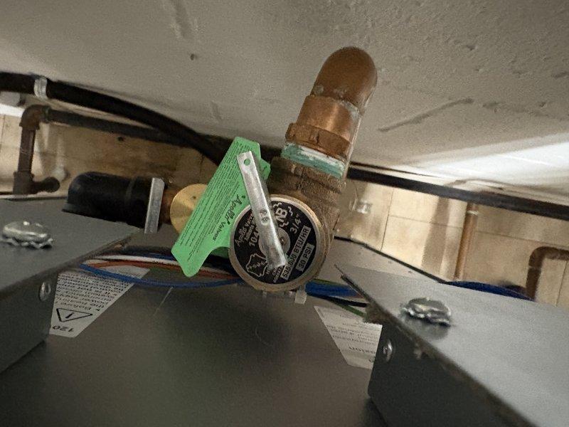 Responded to service call for boiler leak originating from bypass piping on rear of unit. Upon inspection, identified active water leak from corroded copper bypass pipe with visible oxidation and deterioration at connection points. Observed pressure gauge and associated fittings showing signs of age and wear. Water had accumulated on floor despite main water supply being shut off to residence, indicating residual pressure in system. Documented condition of affected copper piping, brass fittings, and pressure monitoring equipment with photographic evidence showing extent of corrosion and leak source location.