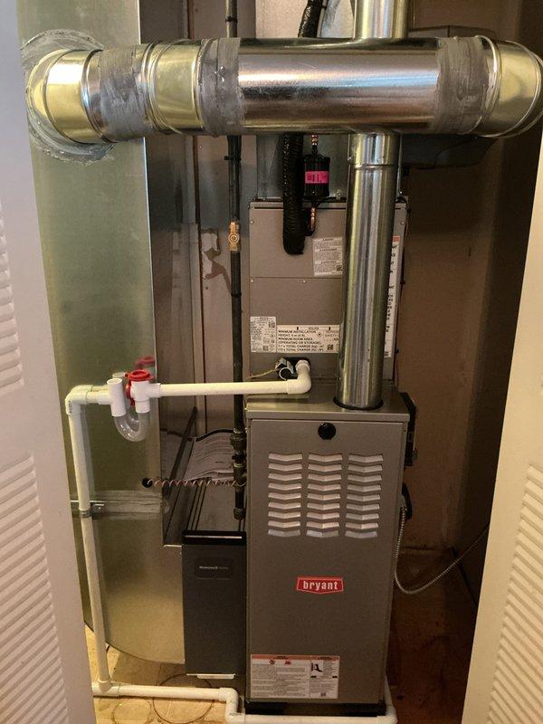 Completed full HVAC system installation including Bryant furnace, outdoor condensing unit, and humidifier in residential property. Installed furnace in interior mechanical room with proper venting and ductwork connections, including horizontal trunk line integration and condensate drainage system using white PVC piping with appropriate fittings. Mounted outdoor Puron-compatible air conditioning condenser unit on concrete pad adjacent to brick exterior, connected refrigerant lines, and verified proper electrical connections. All components installed per manufacturer specifications with appropriate clearances and code compliance. System tested and operational.