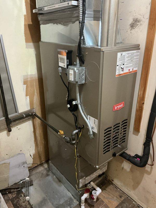 Completed installation of Bryant Preferred Series complete HVAC system including new furnace and air conditioning condenser unit. The furnace was installed in the basement utility area with proper venting, electrical connections via flexible and rigid conduit, and integrated ductwork connections to the existing air distribution system. The outdoor condensing unit was positioned on a level pad with gravel base against the building exterior, with refrigerant lines and electrical service routed through the wall and properly secured. All equipment was installed per manufacturer specifications, electrical connections were made to code, and the system was tested for proper operation.