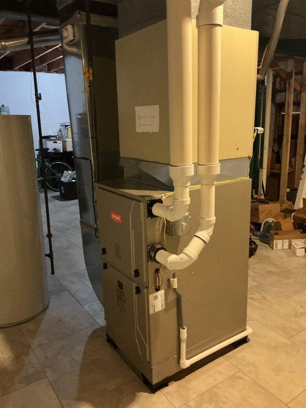 Completed installation of new gas furnace in residential basement utility room. Unit was positioned on tiled floor with proper clearances, connected white PVC intake and exhaust venting routed vertically through ceiling joists, and terminated venting system through exterior wall with appropriate horizontal termination and weather protection. All installations meet code requirements for combustion air and venting specifications.