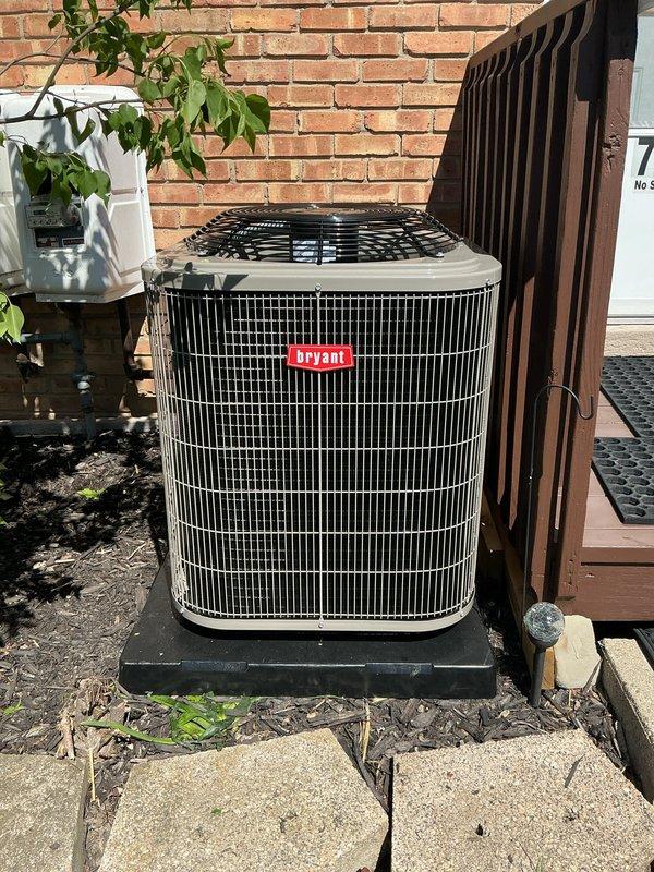 Completed installation of new Bryant air conditioning system including outdoor condenser unit and indoor evaporator coil. Mounted outdoor condenser on level pad against exterior brick wall with proper clearances for airflow and serviceability. Connected refrigerant lines between outdoor unit and indoor coil positioned above existing furnace in basement utility area. Installed electrical disconnect and completed all power wiring to condenser unit and air handler. Verified proper refrigerant charge, tested system operation through complete cooling cycle, and confirmed all connections are secure and leak-free. System is operational and cooling efficiently.