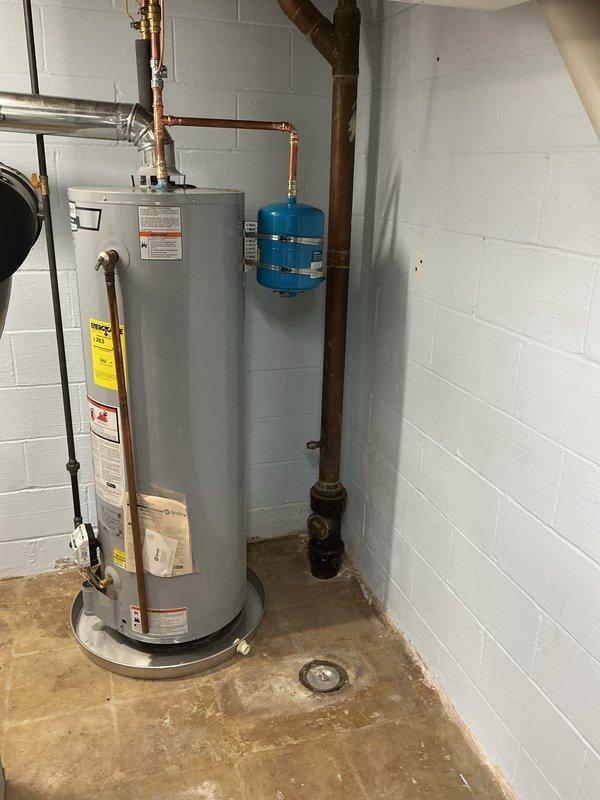 Successfully relocated an AO Smith gas water heater to a new position within the basement utility area. The existing unit was drained completely and disconnected from all supply lines before being moved to the designated location against the white painted concrete block wall.

Installed new copper water supply piping with brass fittings to connect the relocated water heater to the home's plumbing system. A blue expansion tank was mounted to the wall and integrated into the cold water supply line using copper piping and appropriate fittings. All copper connections were properly soldered and pressure tested to ensure leak-free operation.

Reconfigured the gas supply line using black iron piping to reach the new water heater location. All gas connections were completed with approved fittings and tested for leaks using soap solution prior to system activation.

Installed new 4-inch diameter metal venting from the top of the water heater, routing it upward to connect with the existing chimn