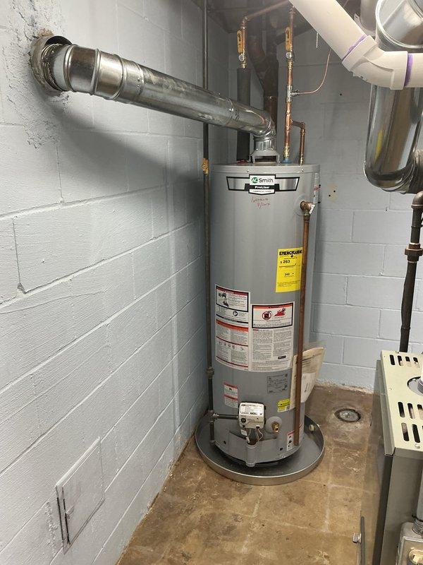 Successfully relocated an AO Smith gas water heater to a new position within the basement utility area. The existing unit was drained completely and disconnected from all supply lines before being moved to the designated location against the white painted concrete block wall.

Installed new copper water supply piping with brass fittings to connect the relocated water heater to the home's plumbing system. A blue expansion tank was mounted to the wall and integrated into the cold water supply line using copper piping and appropriate fittings. All copper connections were properly soldered and pressure tested to ensure leak-free operation.

Reconfigured the gas supply line using black iron piping to reach the new water heater location. All gas connections were completed with approved fittings and tested for leaks using soap solution prior to system activation.

Installed new 4-inch diameter metal venting from the top of the water heater, routing it upward to connect with the existing chimn