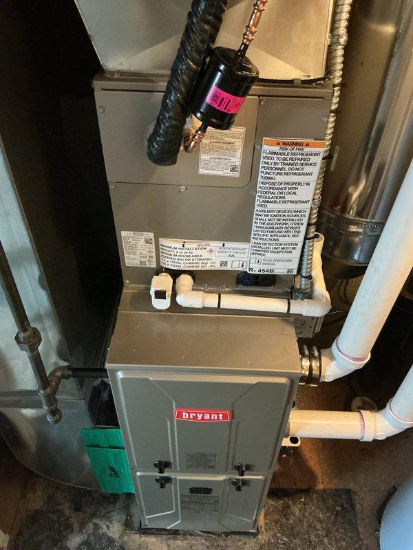 Completed full HVAC system installation including new Bryant furnace and air conditioning condenser unit. Installed outdoor condensing unit on pad with proper grounding, connected refrigerant lines with insulation, established electrical connections with disconnect box, and routed PVC condensate drainage. Indoor installation included furnace placement, air handler/plenum assembly, refrigerant line connections, and metal ductwork integration with proper insulation. All components mounted on concrete foundation, system tested and verified operational.