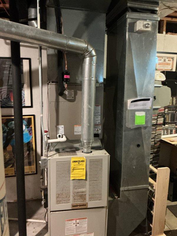 Completed installation of new air conditioning system including outdoor condenser unit and indoor evaporator coil. Outdoor unit was positioned on drain pan next to building foundation with proper clearance from structure and landscaping. Indoor evaporator coil was installed above existing furnace in basement mechanical room, integrated with existing ductwork system. All refrigerant lines were connected, system was charged to manufacturer specifications, electrical connections were completed, and unit was tested for proper operation and airflow.