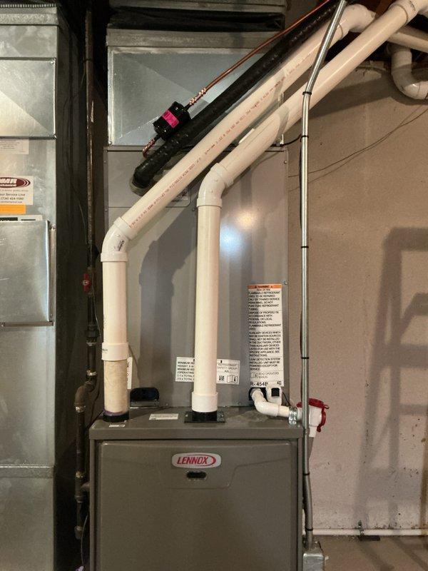 Completed installation of new Bryant air conditioning condenser unit and evaporator coil system. The outdoor condenser was positioned on a level gravel pad against the home's exterior with proper clearances maintained for airflow and serviceability. Inside the residence, installed the new evaporator coil in conjunction with the existing Lennox furnace, establishing refrigerant line connections between indoor and outdoor components. Installed PVC intake and exhaust venting with proper routing and support, completed all electrical connections to the control box mounted on exterior wall, and pressure-tested the refrigerant system to verify leak-free operation before final charging to manufacturer specifications.