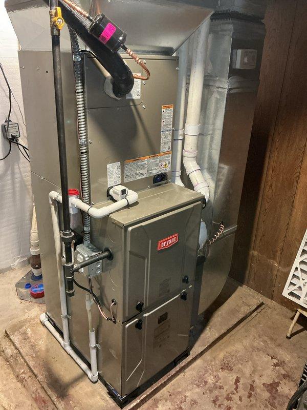 Completed full HVAC system installation including Bryant furnace, air conditioning condenser unit, and humidifier in residential property. Installed furnace in basement mechanical room with proper venting via white PVC piping, established electrical connections with flexible metallic conduit, and integrated ductwork assembly to air handler section. Mounted outdoor Bryant condenser unit on concrete pad against exterior wall with appropriate clearances, installed electrical disconnect box, and ran conduit from disconnect to unit. Connected refrigerant lines between indoor and outdoor components, installed condensate drainage system, and integrated humidifier into duct system. All equipment installed per manufacturer specifications with proper labeling visible on units. System tested and confirmed operational.