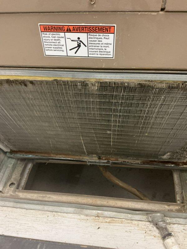 Completed multi-system HVAC tune-up maintenance on two separate rental units. Upon inspection, discovered significant ice buildup on evaporator coil fins with extensive icicle formation along the bottom edge of the unit, indicating restricted airflow and potential refrigerant issues. The coil assembly showed heavy frost accumulation obscuring the metal fins, along with visible dirt and discoloration throughout the heat exchanger. Addressed condensation and freezing conditions affecting system performance. Documented all findings with photographic evidence showing the electrical shock warning labels, copper refrigerant lines, drainage pan area, and the extent of ice formation on the coil assembly. Maintenance performed in confined space installation environment.
