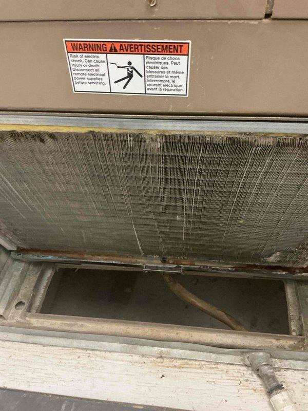 Completed multi-system HVAC tune-up maintenance on two separate rental units. Upon inspection, discovered significant ice buildup on evaporator coil fins with extensive icicle formation along the bottom edge of the unit, indicating restricted airflow and potential refrigerant issues. The coil assembly showed heavy frost accumulation obscuring the metal fins, along with visible dirt and discoloration throughout the heat exchanger. Addressed condensation and freezing conditions affecting system performance. Documented all findings with photographic evidence showing the electrical shock warning labels, copper refrigerant lines, drainage pan area, and the extent of ice formation on the coil assembly. Maintenance performed in confined space installation environment.