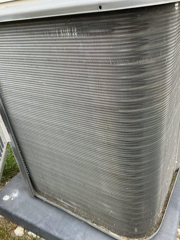 # HVAC Maintenance - Cooling System Service

Performed routine maintenance on outdoor air conditioning condenser unit experiencing reduced cooling efficiency due to significant debris accumulation and environmental contamination. Upon inspection, found substantial dirt, dust, and debris buildup throughout condenser coil fins, with heavy blockage in multiple sections restricting proper airflow and heat exchange capability. Observed green moss and algae growth at unit base, dirt streaking on exterior casing, and general weathering consistent with extended operation without maintenance.

Thoroughly cleaned condenser coil fins to remove accumulated debris and restore optimal airflow through heat exchange surfaces. Addressed contamination blocking fin spacing to ensure proper system operation and efficiency. Cleaned exterior surfaces and removed biological growth from unit base and mounting area. Verified refrigerant line connections and inspected electrical disconnect for proper operation.