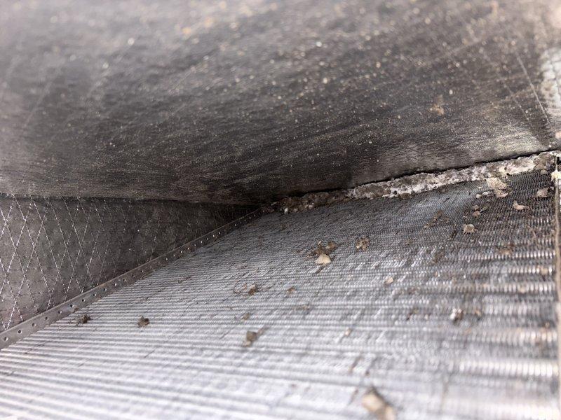Responded to a warranty callback for water leak underneath furnace unit following recent GFCI replacement. Upon inspection, discovered water accumulation beneath the air handler with visible moisture and debris buildup at component seams and heat exchanger surfaces. Documented conditions with photos showing the affected areas including the corrugated heat exchanger fins and junction points where water infiltration occurred.