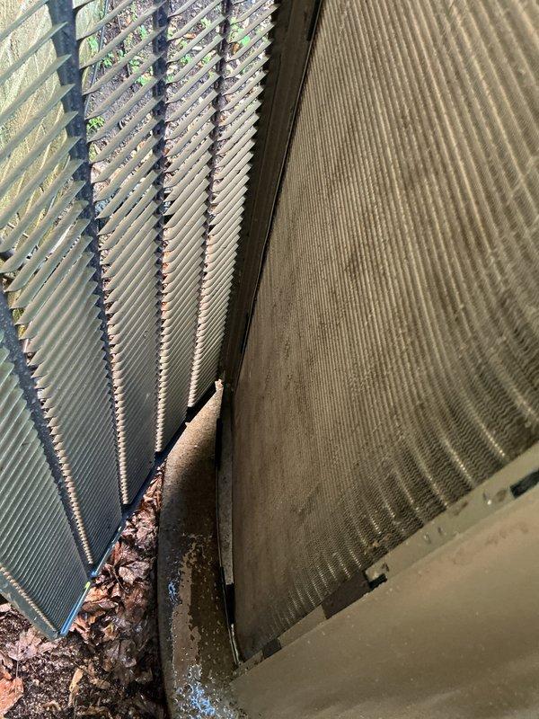 Performed complimentary air conditioning tune-up and system inspection. Documented condenser coil condition showing moderate debris accumulation including leaves and organic material at coil base junction. Observed dust and particulate buildup on air filter media with visible dirt streaking patterns. Evaluated heat exchanger fins for cleanliness and airflow efficiency, noting weathering and discoloration on exterior coil surfaces from outdoor exposure.