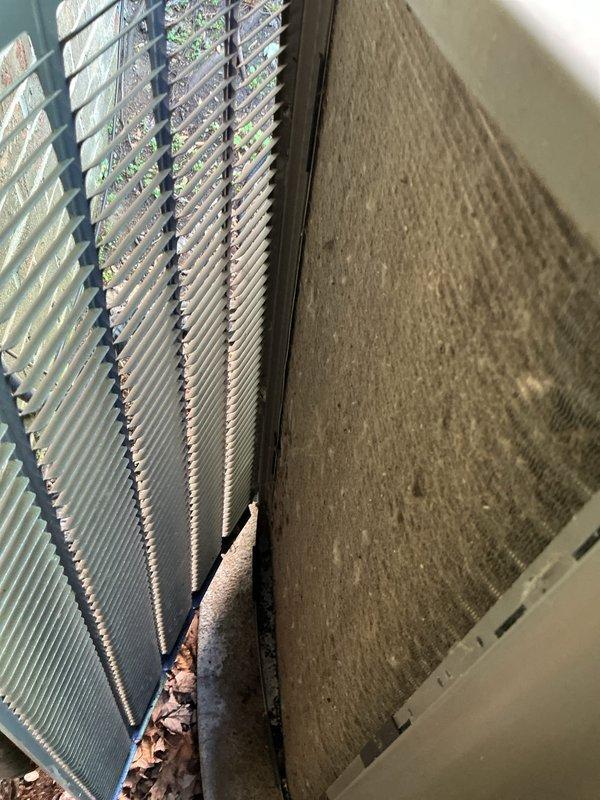 Performed complimentary air conditioning tune-up and system inspection. Documented condenser coil condition showing moderate debris accumulation including leaves and organic material at coil base junction. Observed dust and particulate buildup on air filter media with visible dirt streaking patterns. Evaluated heat exchanger fins for cleanliness and airflow efficiency, noting weathering and discoloration on exterior coil surfaces from outdoor exposure.